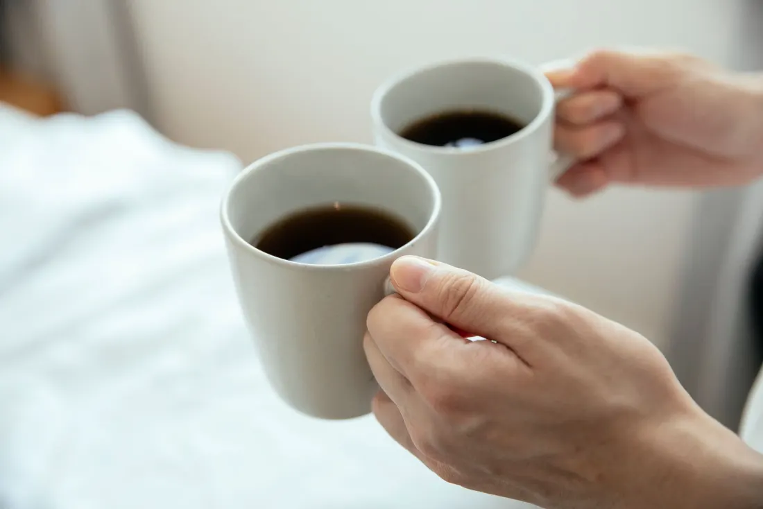 Two hands bringing mugs of coffee together in soft morning light